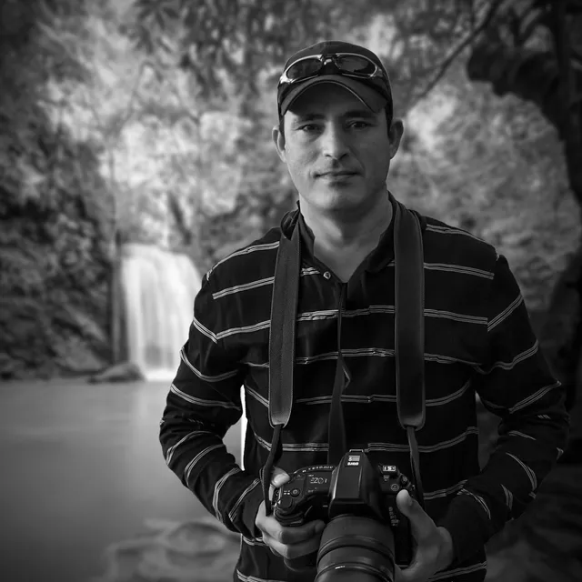 Arnold Petersen holding a camera at a forest waterfall, strap around his neck
