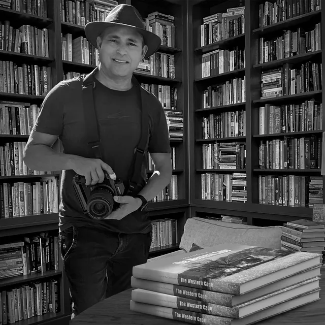 Arnold in a library with camera in hand, copies of The Western Cape stacked on the table