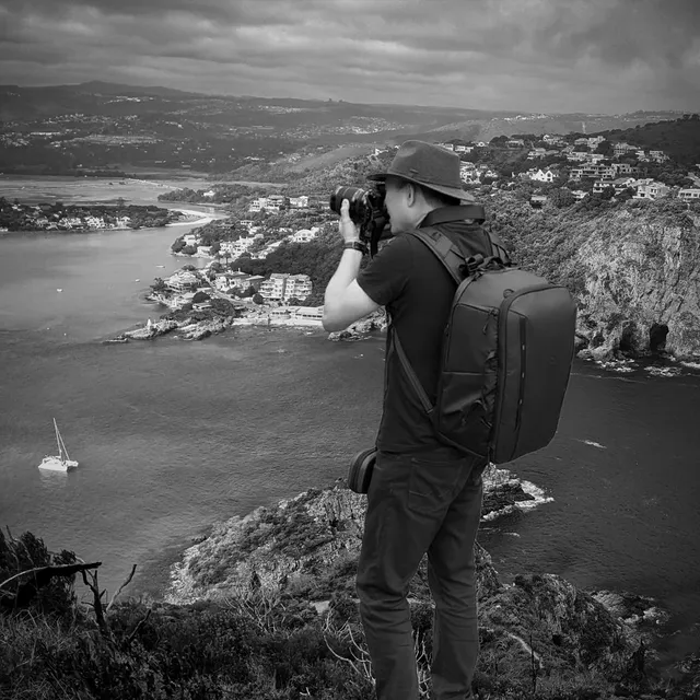 Arnold photographing the Knysna estuary from a headland, camera bag on his back
