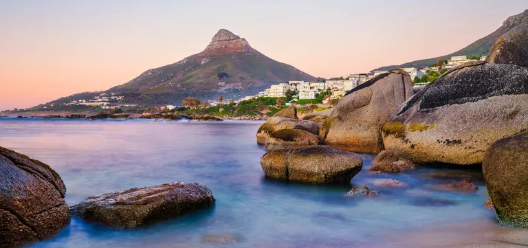 Granite boulders and a quiet cove at dusk with Lion's Head rising behind, Cape Town's Atlantic Seaboard