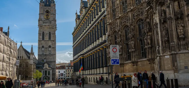 The Belfry rising beyond the Stadhuis, its black-and-gold Renaissance colonnade and Gothic stone wing side by side, people crossing the square