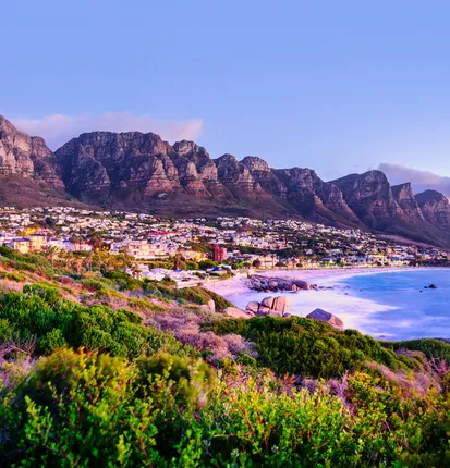 A photograph from the book: Camps Bay at dusk, the Twelve Apostles ridge above the lit town and the pale curve of the beach below