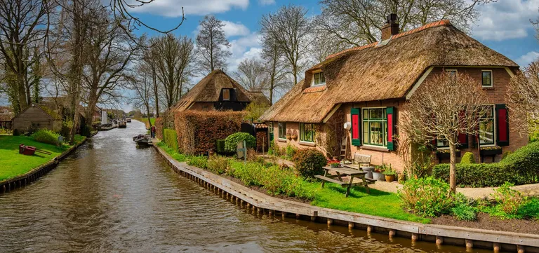 Thatched-roof houses reflected in a still canal in Giethoorn, Netherlands
