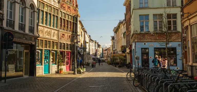 A cobbled street in central Ghent lined with colourful independent shopfronts, bicycles parked along one side