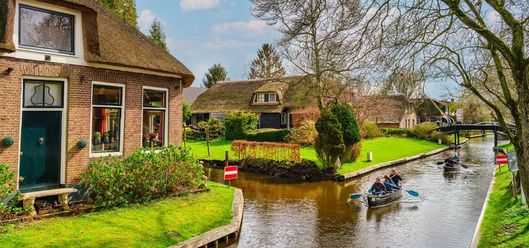 A whisper boat carrying visitors along a Giethoorn canal past thatched houses and gardens