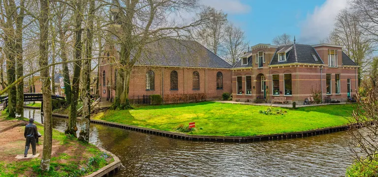 The Albert Mol statue among the trees beside the canal in Giethoorn, a wooden bridge beyond