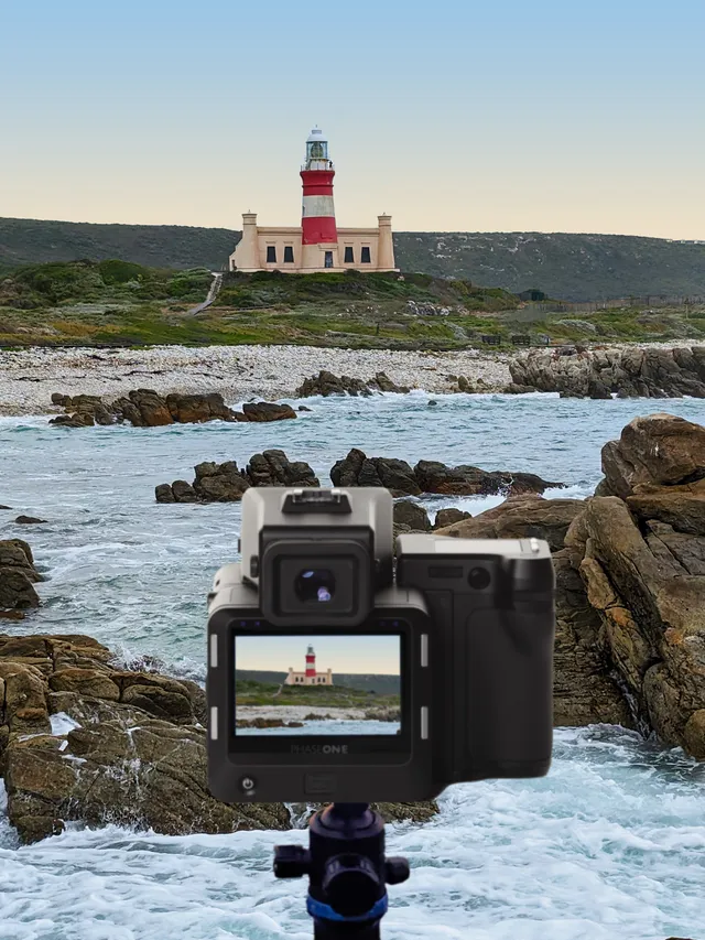 A medium-format camera on a tripod frames the red-and-white striped lighthouse across breaking surf