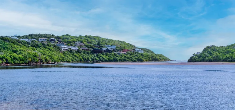 The Swartvlei lagoon meeting the sea past green dune hills at Sedgefield, Garden Route, South Africa