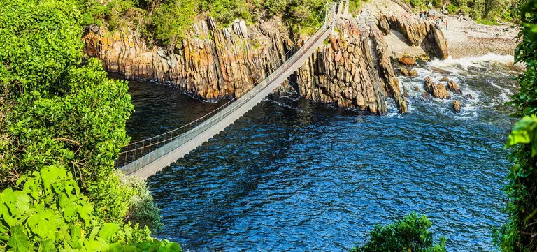 The Storms River Mouth suspension bridge spanning the water beneath rock cliffs in Tsitsikamma National Park, South Africa