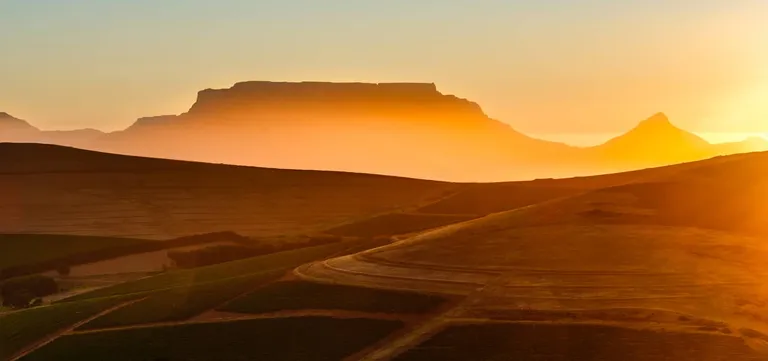 Table Mountain's flat-topped silhouette at sunset beyond rolling vineyard hills outside Cape Town