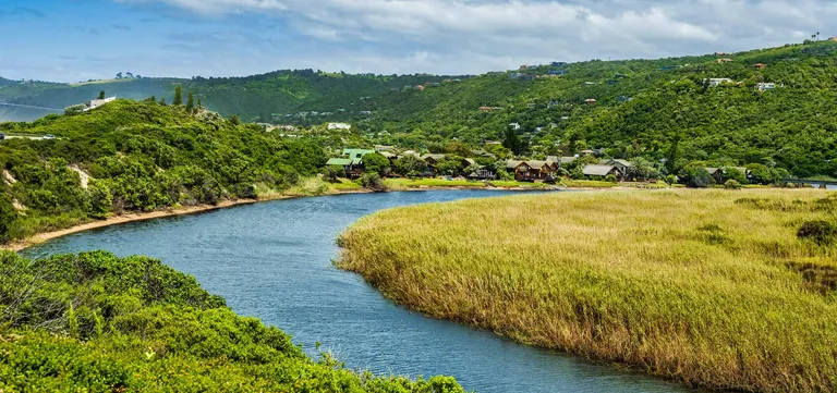 A river bend through golden reed beds past timber chalets in Wilderness, Garden Route, South Africa